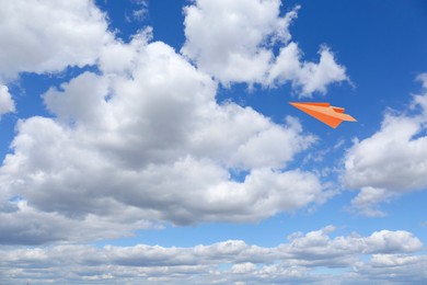 Image of Orange paper plane flying in blue sky with clouds