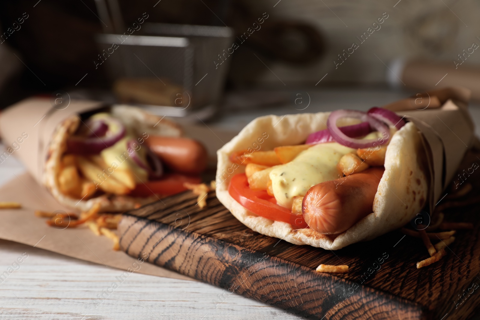 Photo of Delicious pita wrap with sausages, vegetables and potato fries on white wooden table, closeup