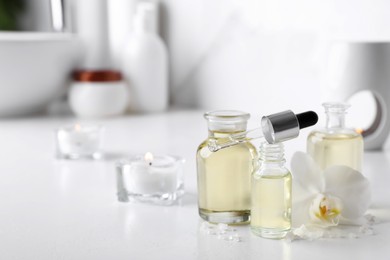 Essential oils, sea salt and orchid flower on white table in bathroom, closeup. Space for text