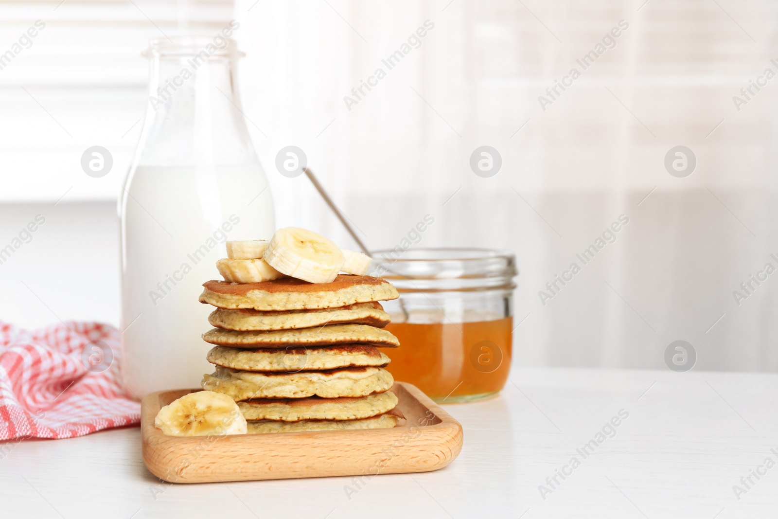 Photo of Plate of banana pancakes with honey and milk on white wooden table. Space for text