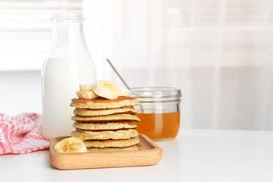 Photo of Plate of banana pancakes with honey and milk on white wooden table. Space for text