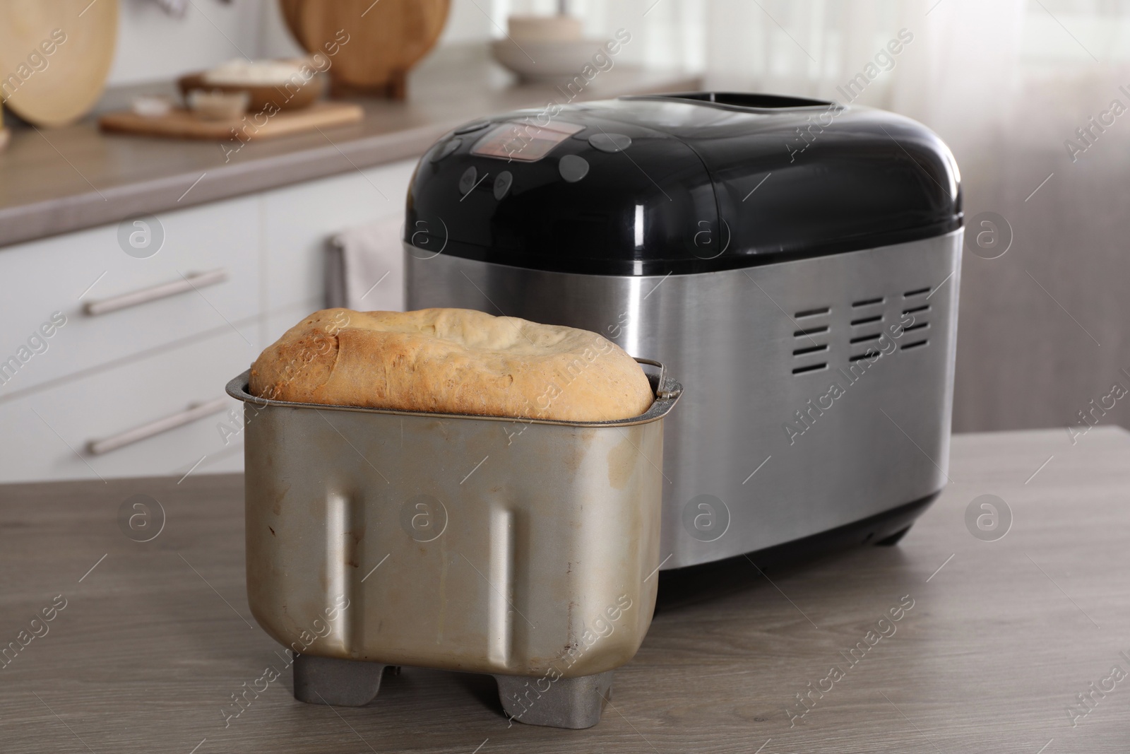 Photo of Breadmaker and fresh homemade bread in pan on wooden table in kitchen