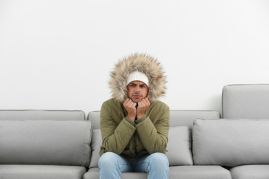 Photo of Young man in warm clothes freezing on sofa against white background