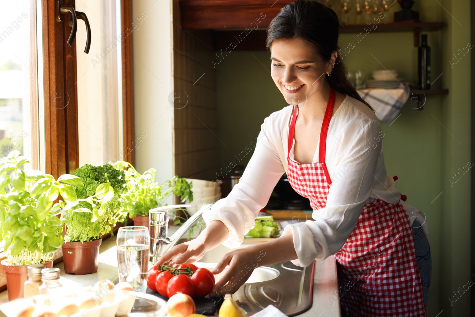 Photo of Young woman with fresh tomatoes at countertop in kitchen