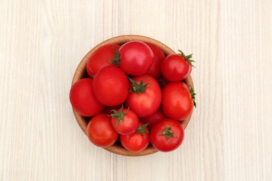 Photo of Bowl of ripe red tomatoes on light wooden table, top view