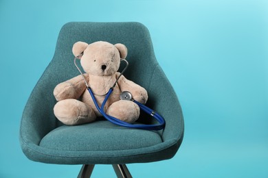 Photo of Teddy bear with stethoscope in armchair on light blue background, space for text. Pediatrician practice