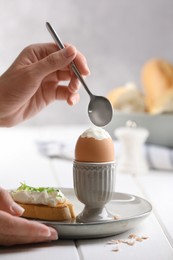 Woman eating fresh soft boiled egg at white wooden table, closeup