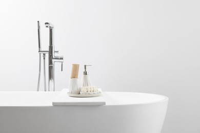 Photo of Different personal care products and accessories on bath tub in bathroom, space for text