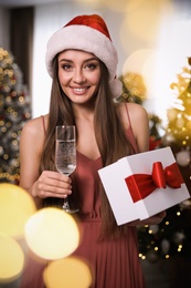 Photo of Beautiful woman in Santa hat with Christmas gift and champagne at home