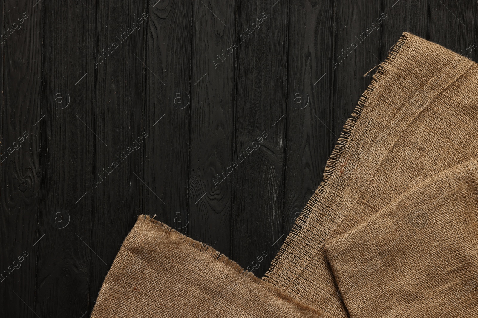 Photo of Burlap fabric on black wooden table, top view. Space for text