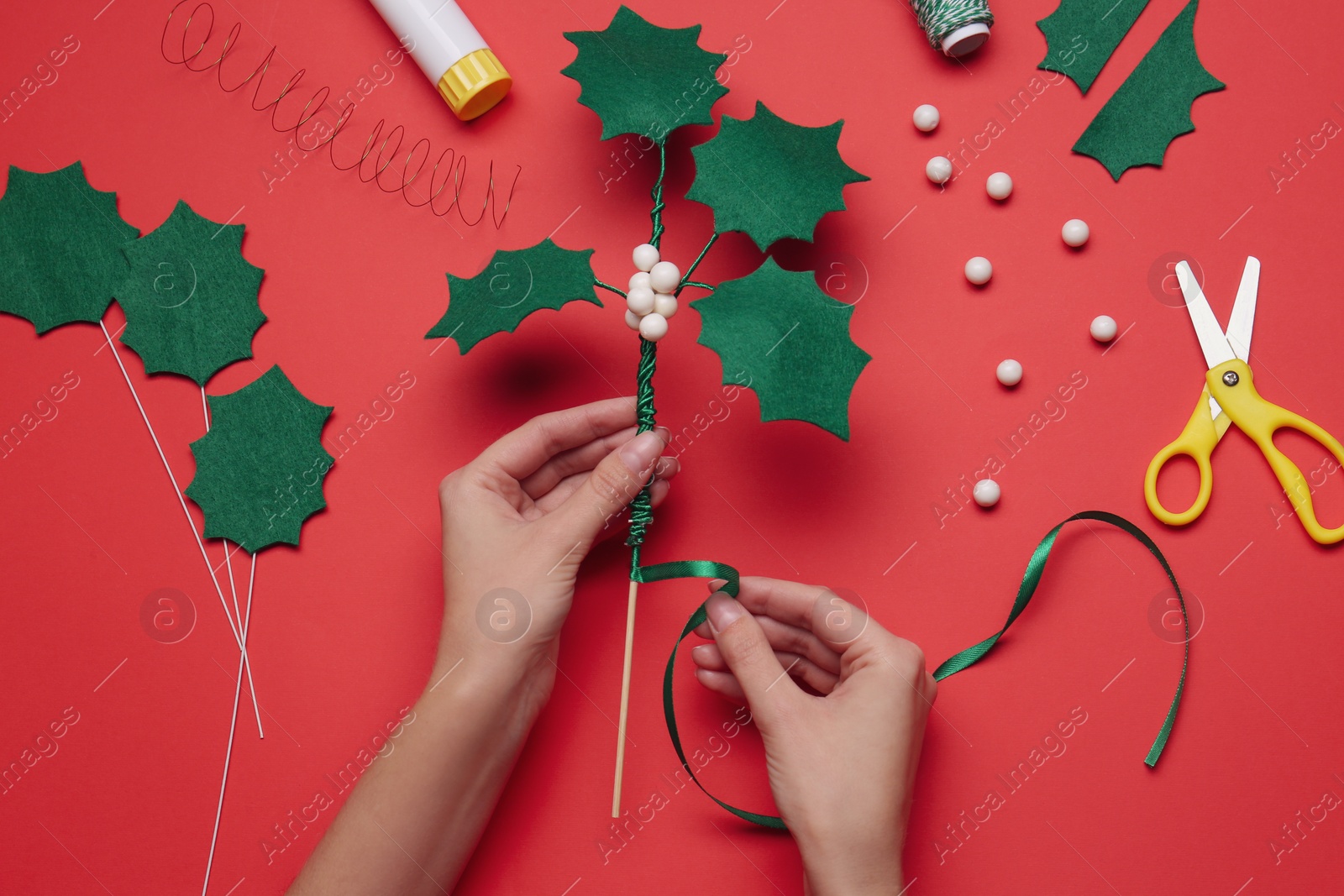 Photo of Woman making mistletoe branch on red background, top view