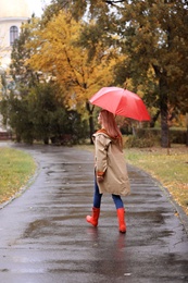 Woman with umbrella taking walk in autumn park on rainy day