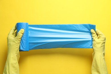Photo of Janitor in rubber gloves holding roll of light blue garbage bags over yellow background, top view