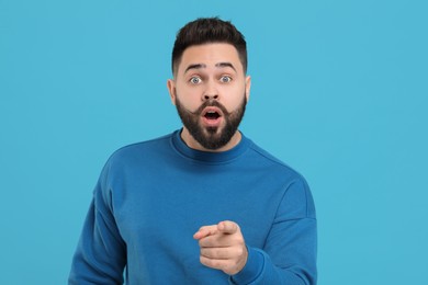 Photo of Surprised young man with mustache pointing at something on light blue background
