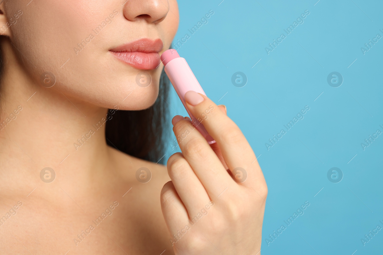 Photo of Young woman applying lip balm on turquoise background, closeup. Space for text