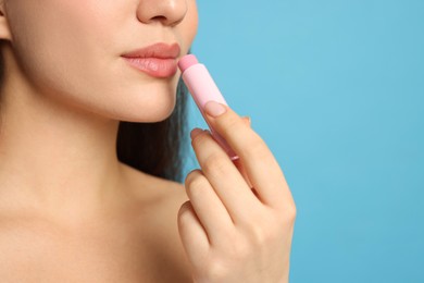 Photo of Young woman applying lip balm on turquoise background, closeup. Space for text