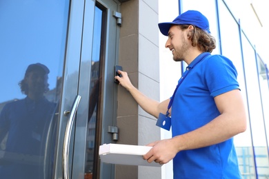 Photo of Male courier with pizza ringing in doorbell at entrance. Food delivery service