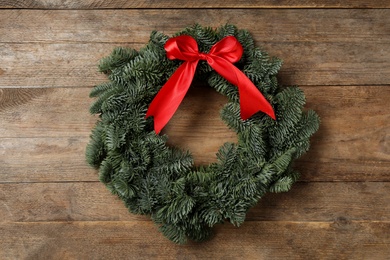 Photo of Christmas wreath made of fir tree branches with red ribbon on wooden background