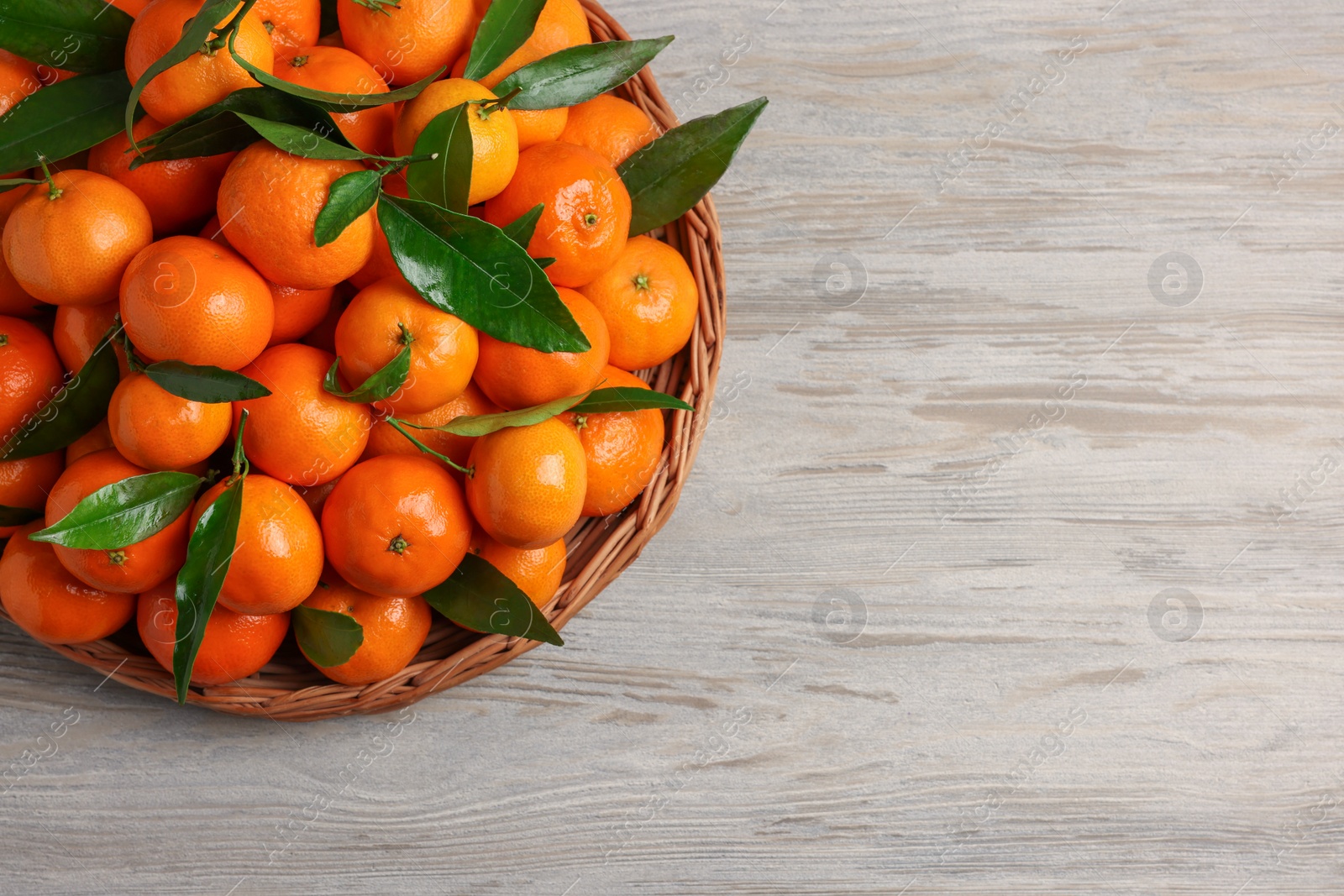 Photo of Ripe juicy tangerines and green leaves on white wooden table, top view. Space for text