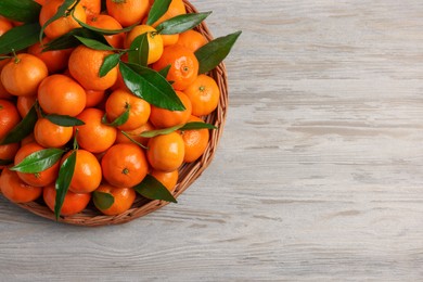 Photo of Ripe juicy tangerines and green leaves on white wooden table, top view. Space for text