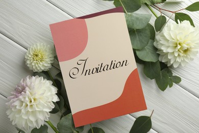 Photo of Card with word Invitation and beautiful flowers on white wooden background, flat lay