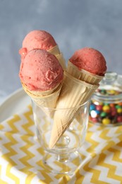 Delicious pink ice cream in wafer cones and candies on white table