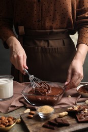 Woman mixing delicious chocolate cream with whisk at table, closeup