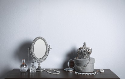 Photo of Small mirror, perfume bottles and jewelry on wooden table near light wall