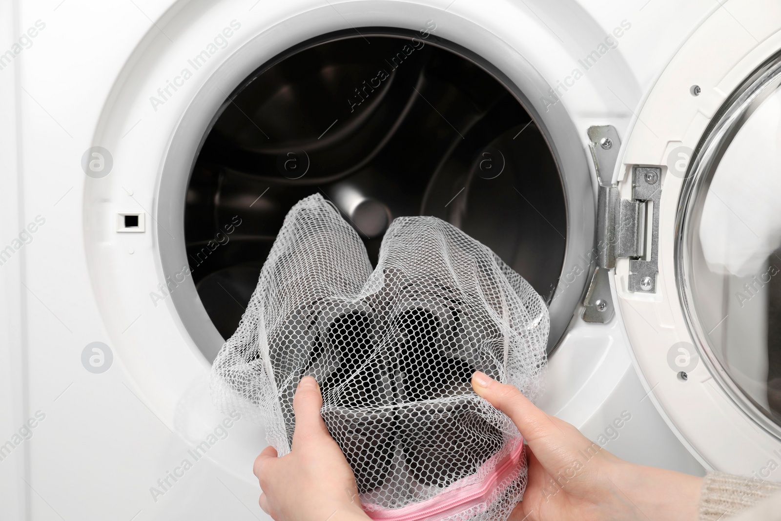 Photo of Woman putting stylish sneakers into washing machine, closeup