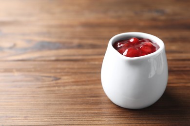 Photo of Fresh cranberry sauce in pitcher on wooden table, closeup. Space for text