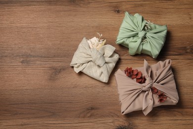 Photo of Furoshiki technique. Gifts packed in fabric and dry leaves on wooden table, flat lay. Space for text