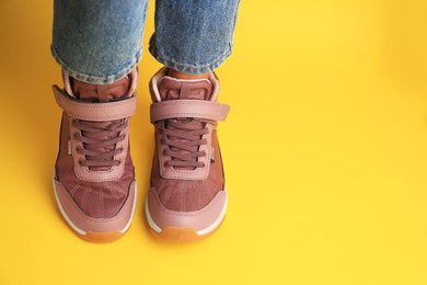 Photo of Girl wearing stylish sneakers on yellow background. Space for text