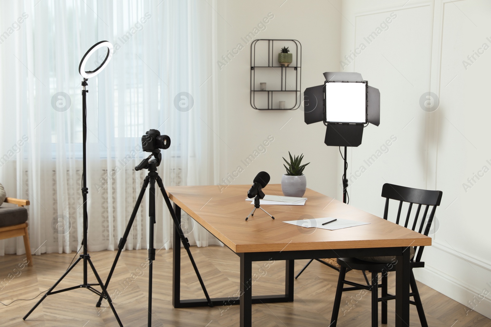 Photo of Camera and lighting equipment on tripods near table in room. Blogger workplace