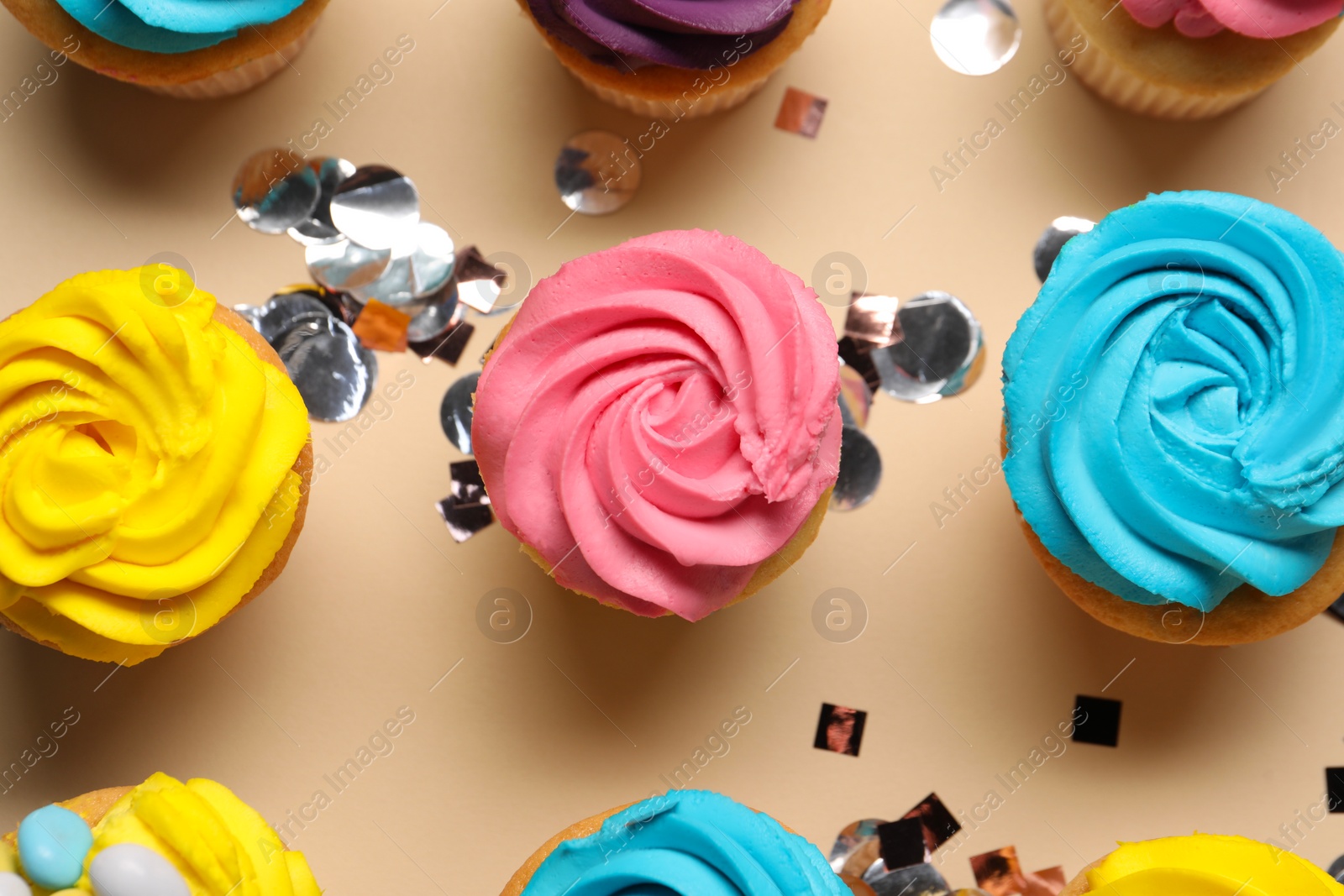 Photo of Delicious cupcakes with bright cream and confetti on beige background, flat lay