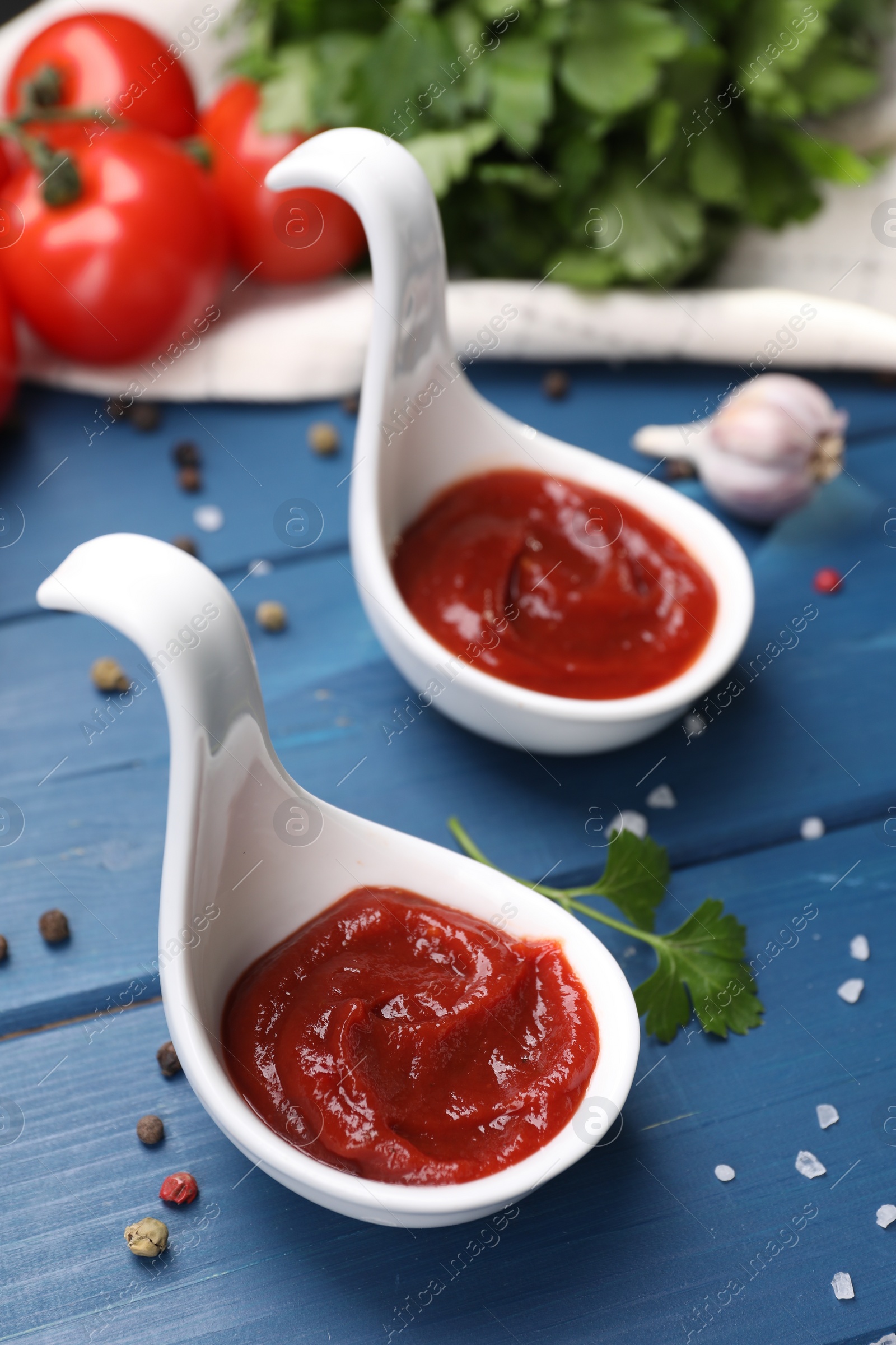 Photo of Organic ketchup in spoons and spices on blue wooden table, closeup. Tomato sauce