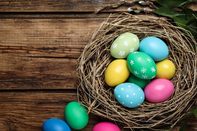 Colorful eggs and nest on wooden background, flat lay with space for text. Happy Easter