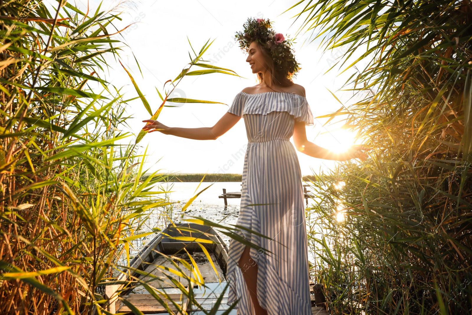 Photo of Young woman wearing wreath made of beautiful flowers near river on sunny day