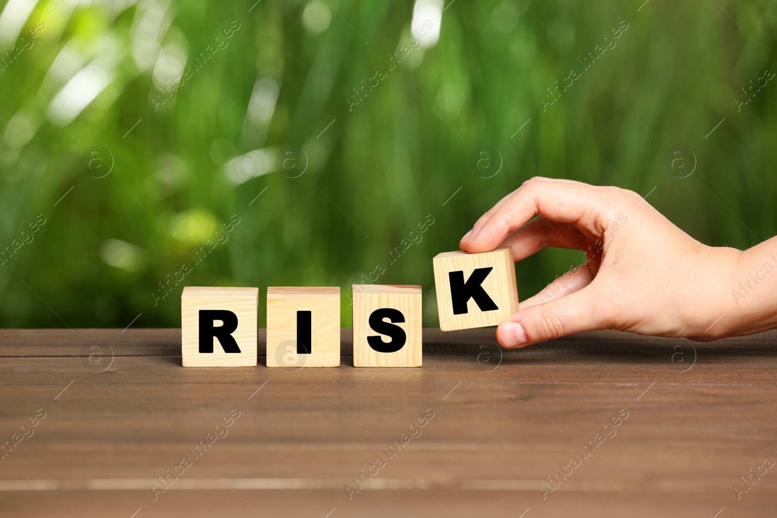 Photo of Woman making word Risk of cubes on wooden table, closeup