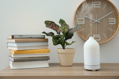 Photo of Aroma oil diffuser, plant and books on wooden table indoors. Interior design