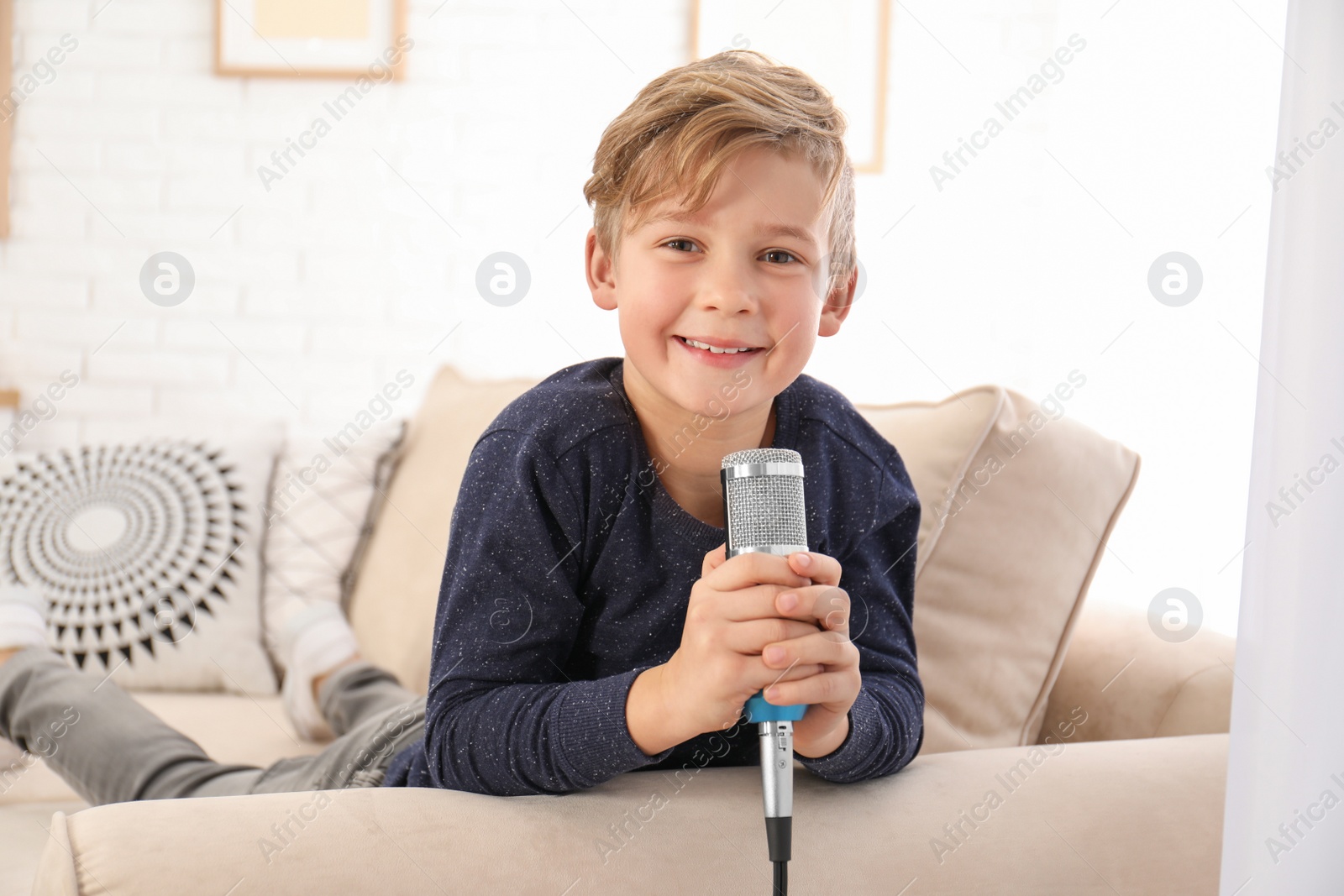 Photo of Cute boy with microphone on sofa in living room