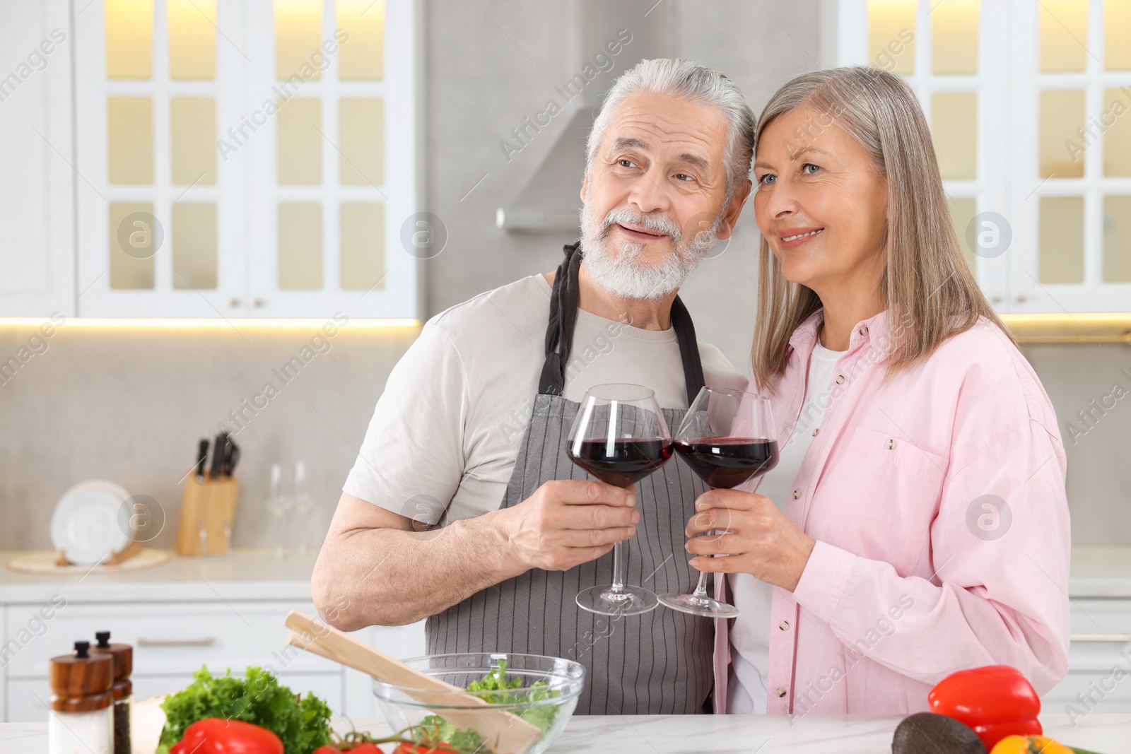 Photo of Happy affectionate senior couple with glasses of wine in kitchen