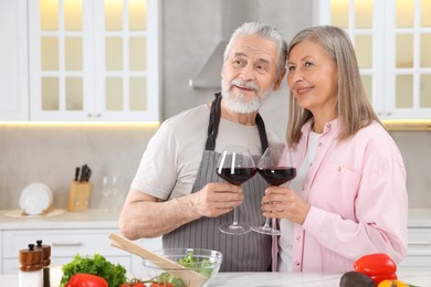 Happy affectionate senior couple with glasses of wine in kitchen