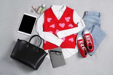 Photo of Pair of stylish red sneakers, clothes, accessories and tablet on light grey fabric, flat lay