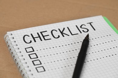 Photo of Notebook with inscription Checklist and pen on kraft surface, closeup