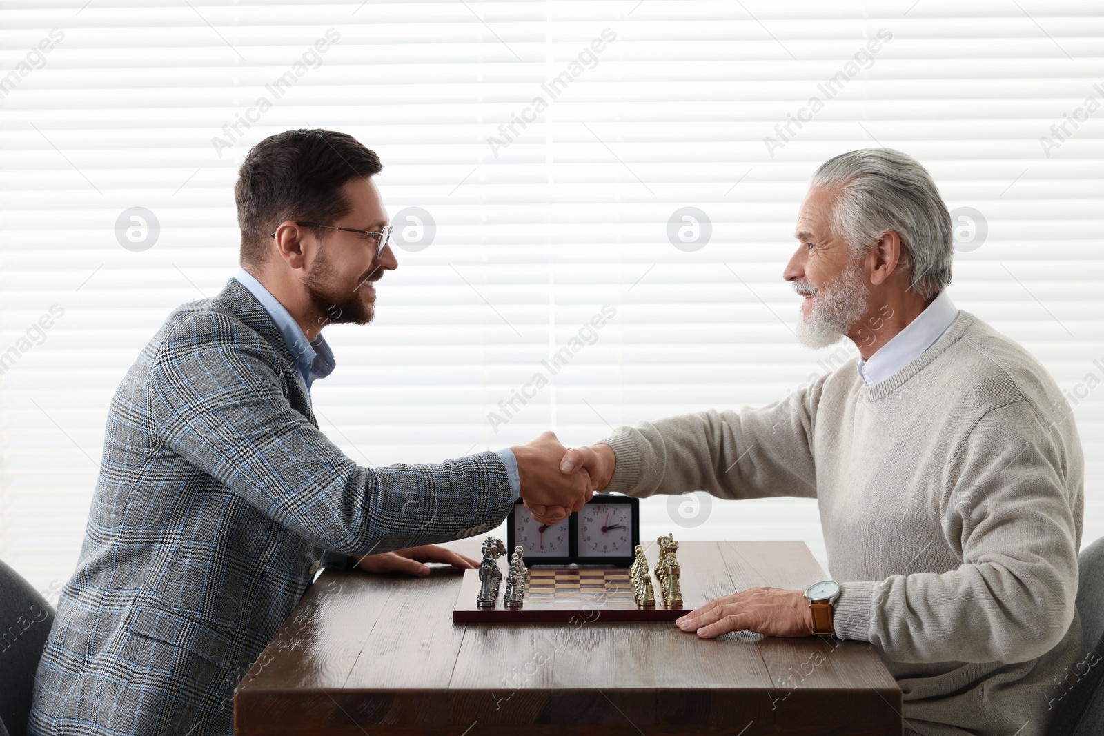 Photo of Men shaking their hands during chess tournament at table indoors