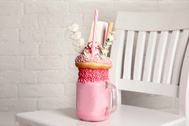 Tasty milk shake with sweets in mason jar on chair near brick wall