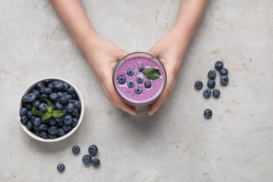 Photo of Woman with tasty blueberry smoothie at light grey table, top view