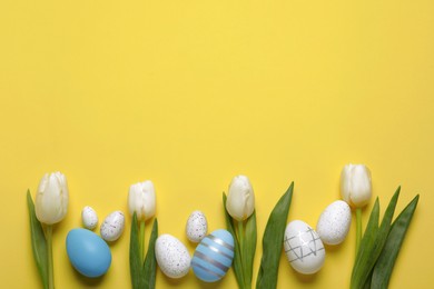 Flat lay composition of painted Easter eggs and tulip flowers on yellow background. Space for text