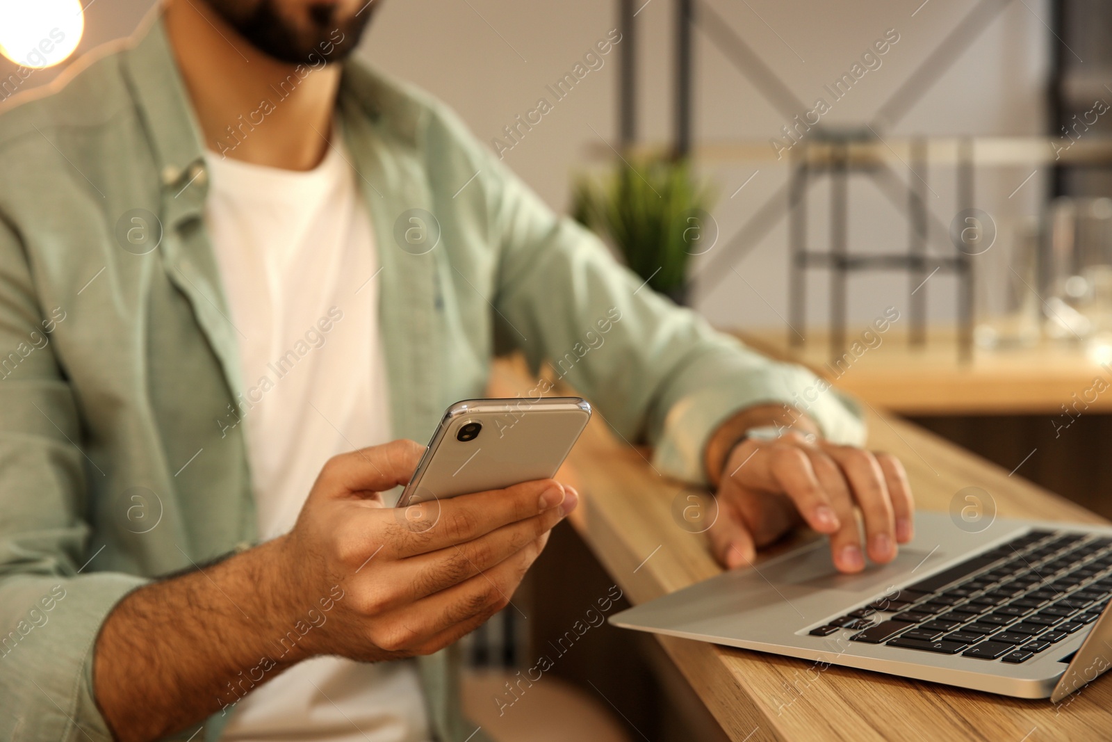 Photo of Man using smartphone while working with laptop in cafe, closeup