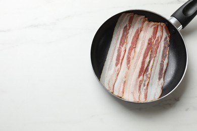 Photo of Slices of raw bacon in frying pan on white marble table, top view. Space for text